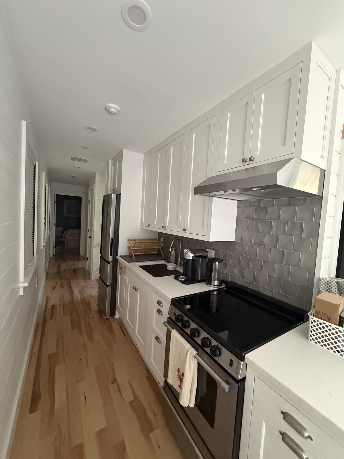 Narrow galley kitchen with white cabinets, grey subway tile backsplash and a stainless range, degreased and wiped down after a deep clean