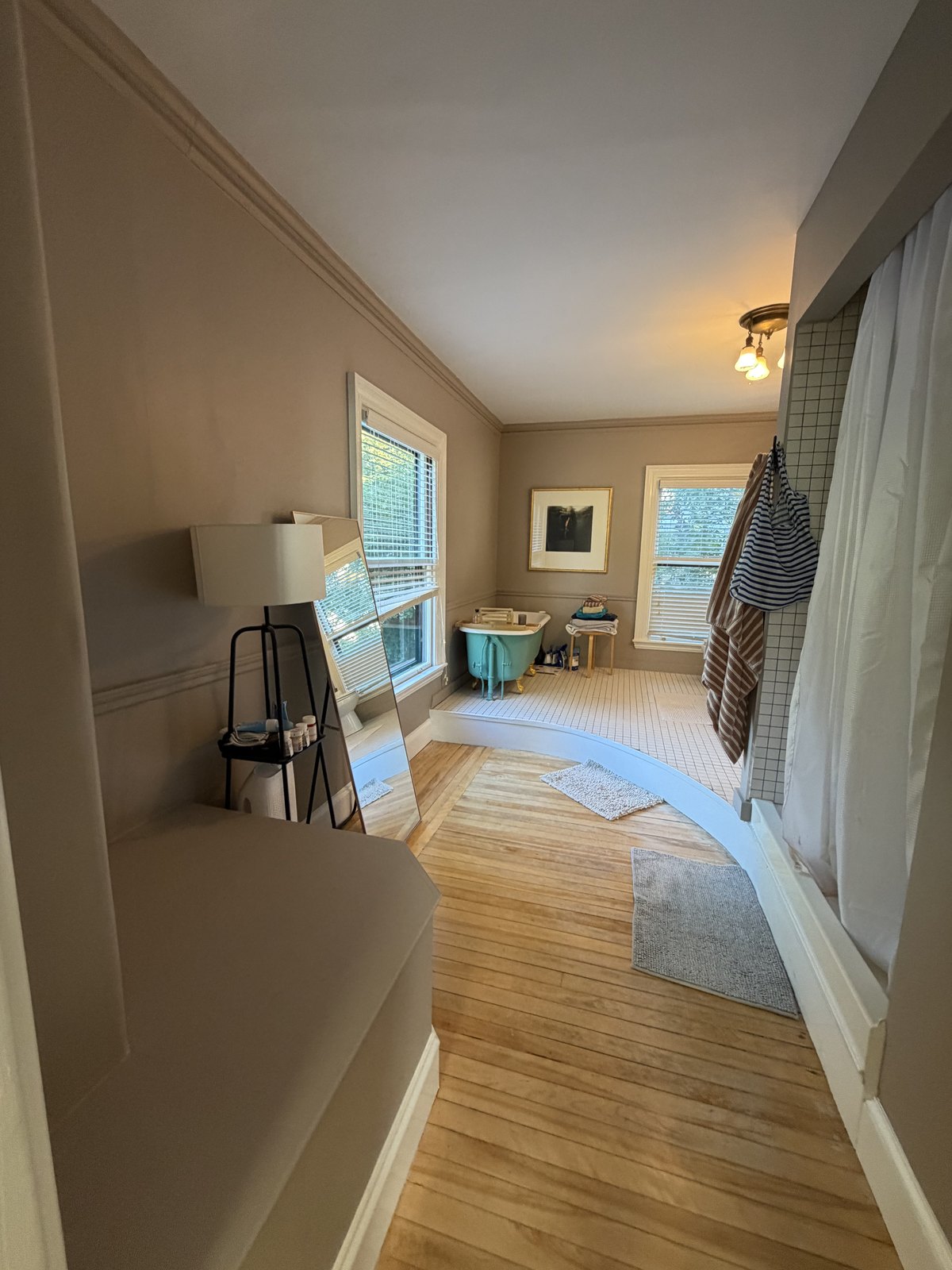 Master bathroom with hardwood floors, a tiled tub platform and a clawfoot tub, with bath mats squared and towels hung after cleaning