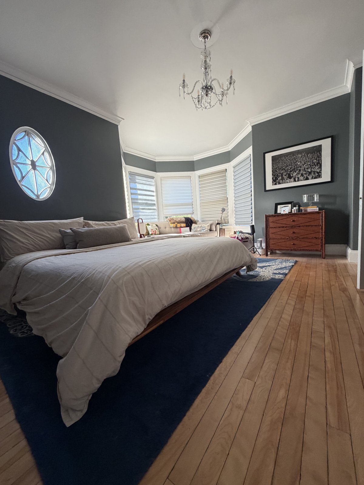 Bedroom with dark green walls, a bay window and a made king bed on a navy rug after a house cleaning visit