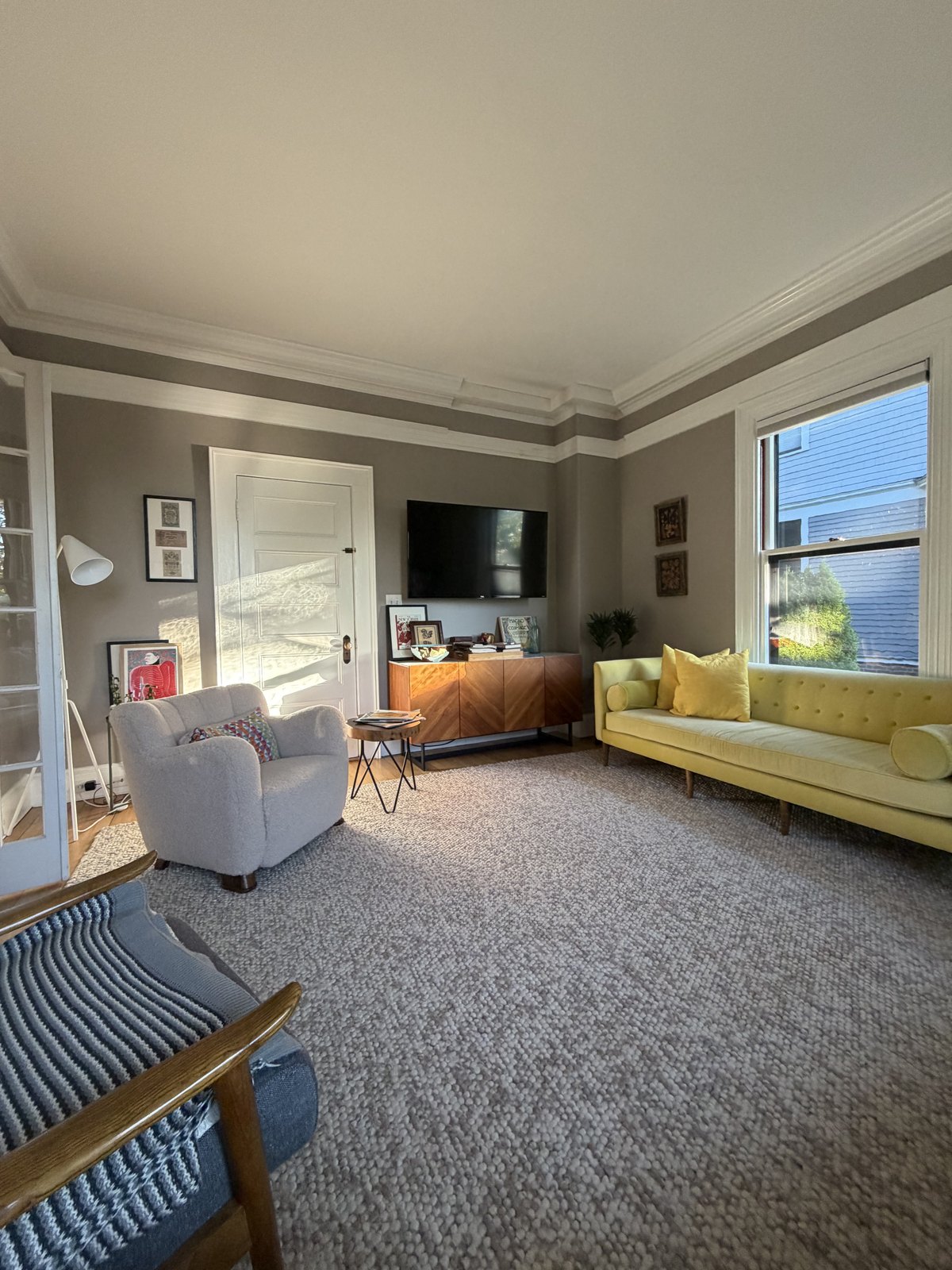 Family room with a yellow sofa, wall-mounted television and a large wool rug, vacuumed and dusted after a house cleaning visit