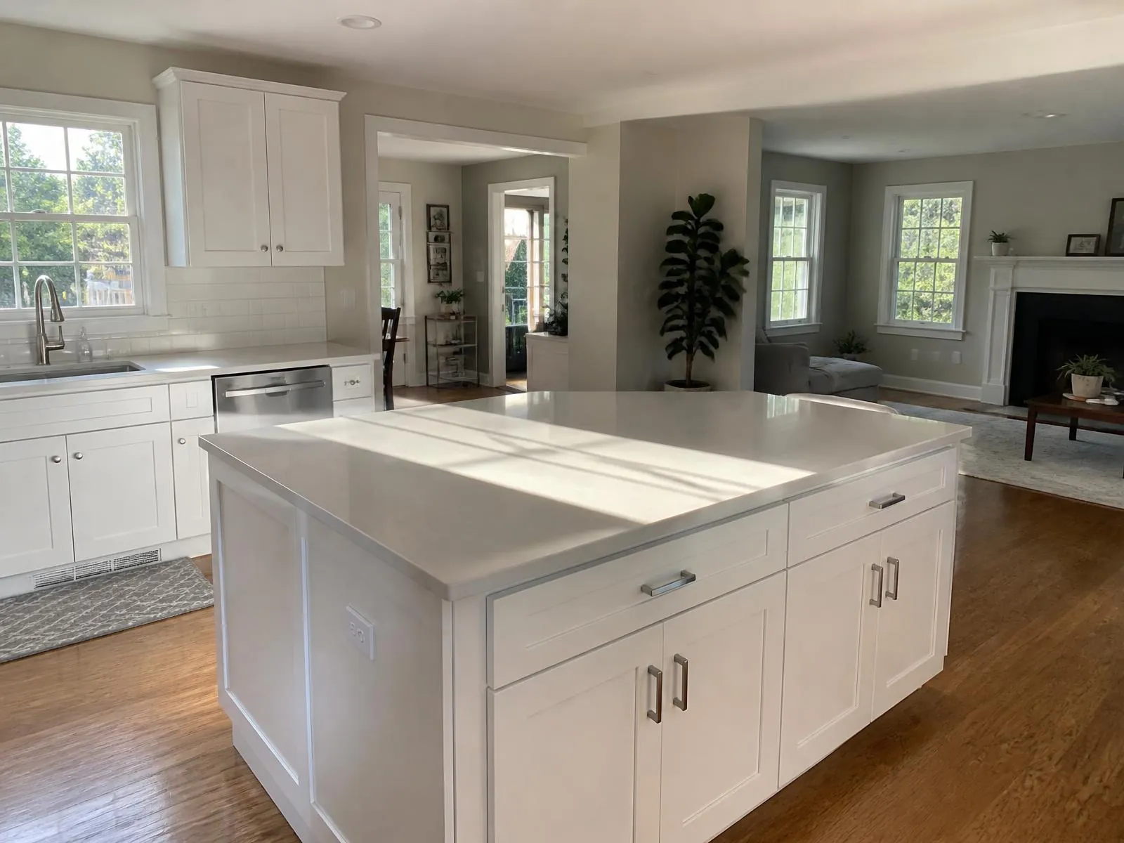 Sunlit open-plan kitchen and living room in a New England home after cleaning, with clear white quartz countertops and hardwood floors