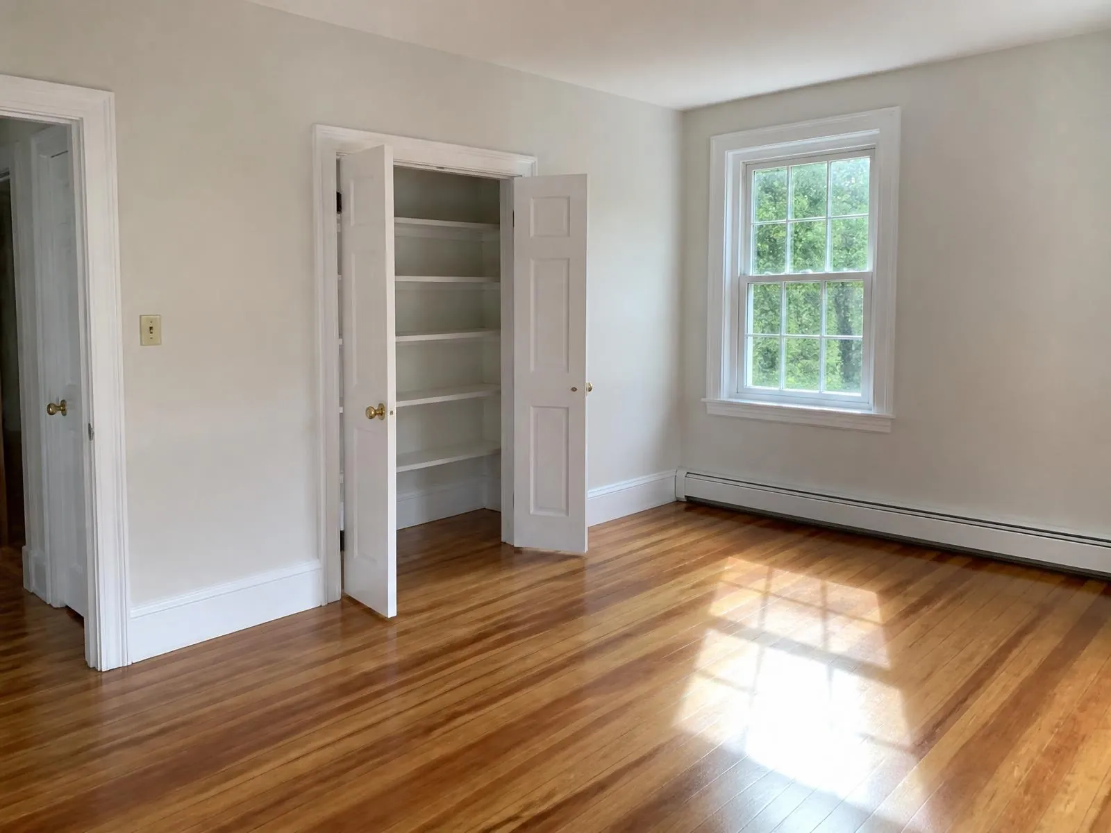Empty bedroom with bare polished hardwood floors, white trim and open closet doors showing wiped shelves